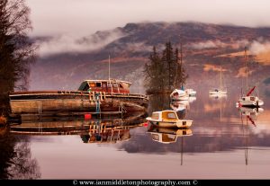 Misty morning reflections of Loch Ness in Scotland. Boats reflected as the morning mist dissipates near Fort Augustus.